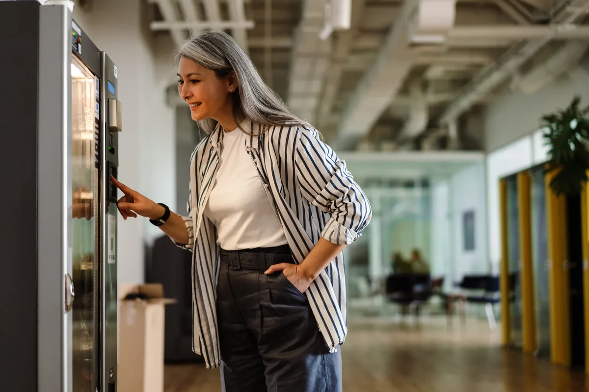 Smiling woman using a vending machine in a bright modern office